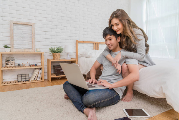 glückliches asiatisches Paar plant und bucht das Hotel für Reisen mit Technologie-Laptop auf dem Schlafzimmerbett im modernen Zuhause, Lebensstil und Reisekonzept, - Foto, Bild