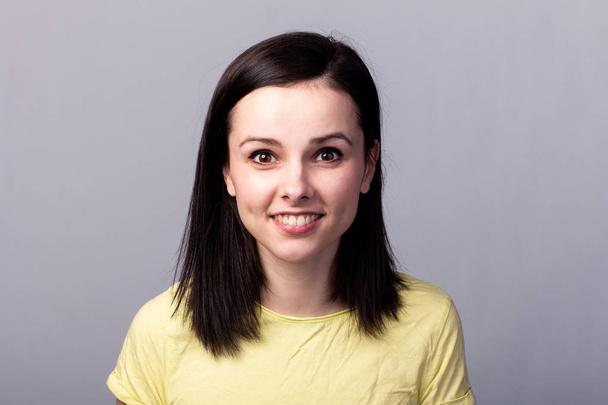 young emotional girl in a yellow t-shirt on a gray background - Photo, Image