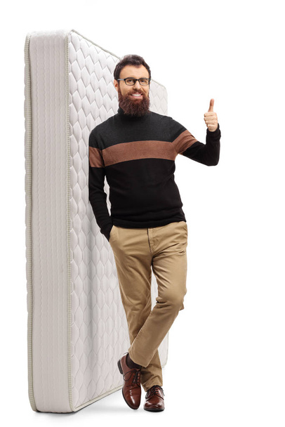 Bearded guy showing thumbs up and leaning on a mattress - Fotografie, Obrázek