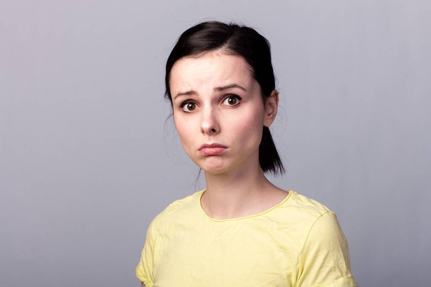 young emotional girl in a yellow t-shirt on a gray background - Foto, imagen