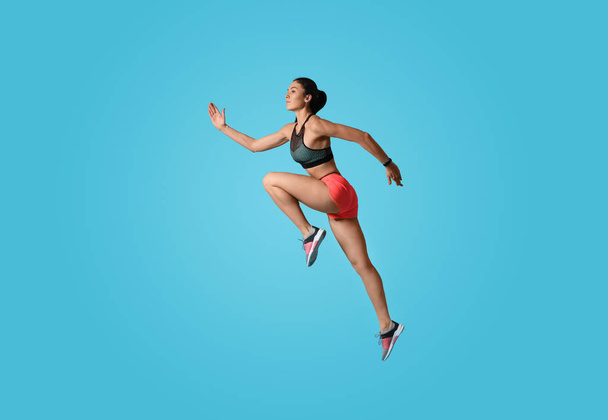 Athletic young woman running on light blue background, side view - Foto, immagini