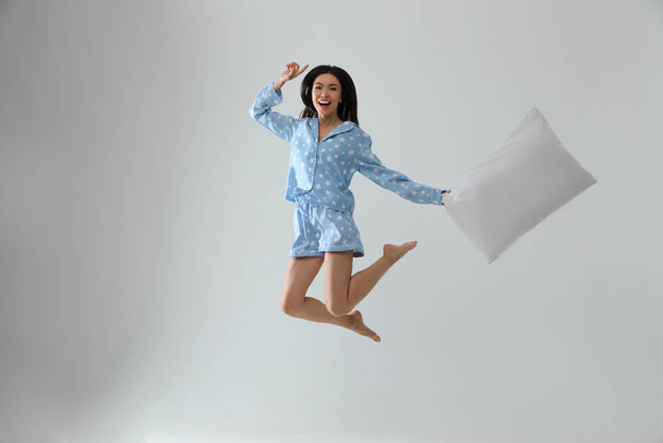 Beautiful Asian woman with pillow jumping on light grey backgrou - Фото, изображение