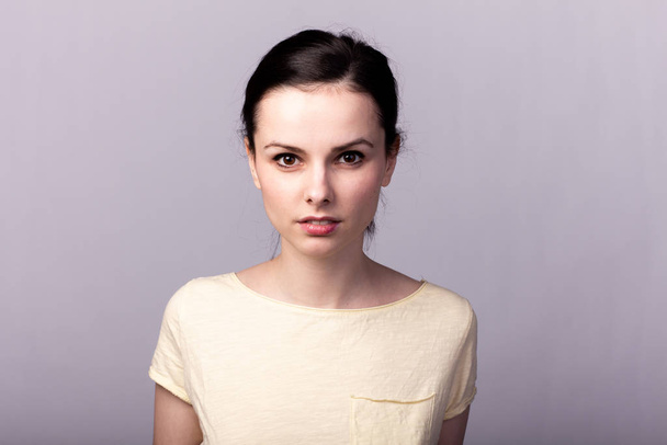 young emotional girl in a yellow t-shirt on a gray background - Фото, изображение
