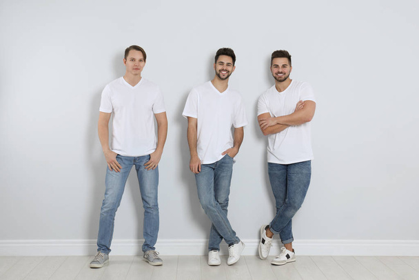 Group of young men in stylish jeans near light wall - Photo, Image