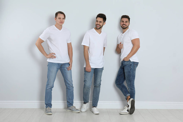Skupina mladých mužů ve stylových džínách u světlé stěny - Fotografie, Obrázek
