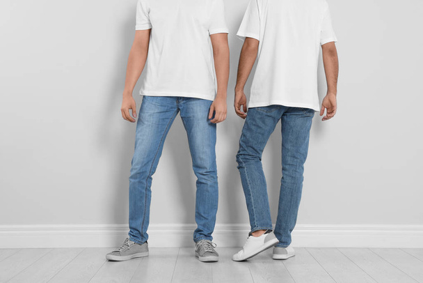 Young men in stylish jeans near light wall, closeup - Foto, Imagem