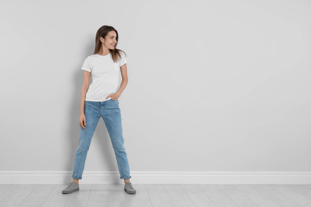 Young woman in stylish jeans near light wall. Space for text - Valokuva, kuva
