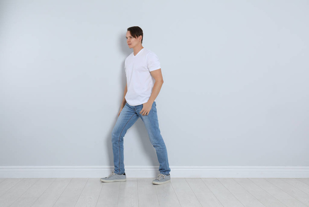 Young man in stylish jeans near light wall - Fotoğraf, Görsel