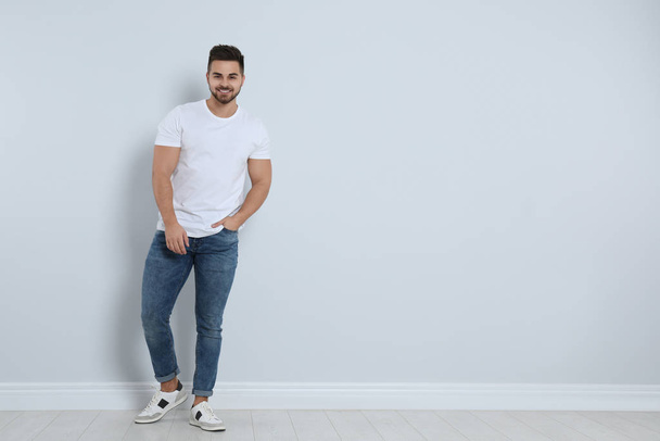 Young man in stylish jeans near light wall. Space for text - Fotografie, Obrázek