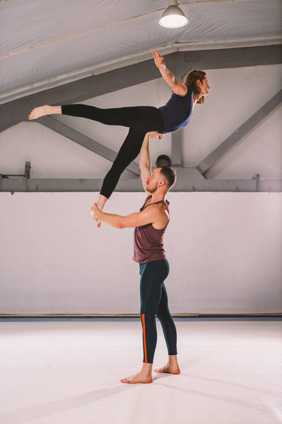 The theme of Acroyoga and Yoga Poses. A pair of two men and a woman stand in the position of asana. The guy holds the girl arched high back on the outstretched arm. In the gym with a studio Backlight - Foto, immagini