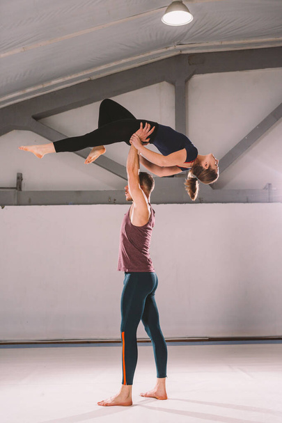 The theme of Acroyoga and Yoga Poses. A pair of two men and a woman stand in the position of asana. The guy holds the girl arched high back on the outstretched arm. In the gym with a studio Backlight - Fotó, kép