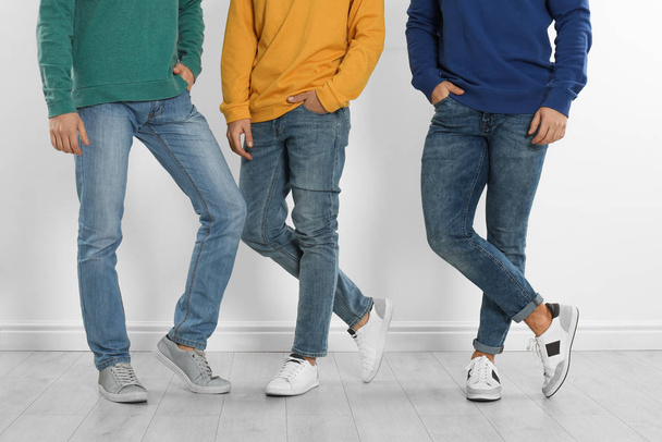 Group of young men in stylish jeans near white wall, closeup - Photo, Image