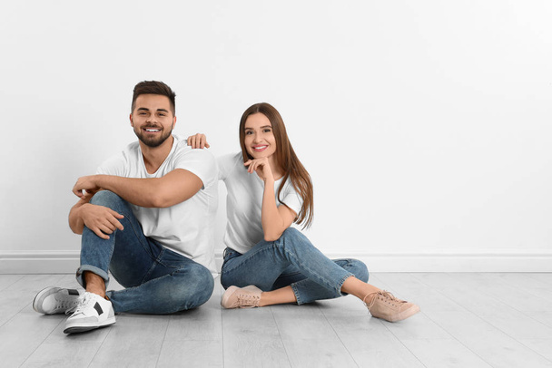 Young couple in stylish jeans sitting near white wall - Фото, зображення