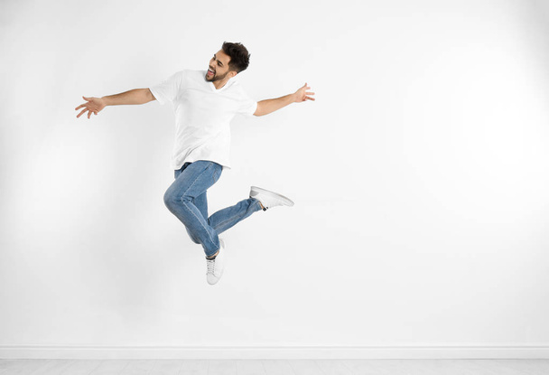 Jovem em jeans elegantes pulando perto da parede branca
 - Foto, Imagem