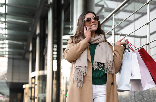 Beautiful young woman with shopping bags talking on smartphone o - Photo, image