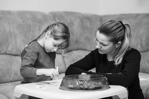 sechsjähriges kaukasisches Mädchen beim Spielen schmelzbarer bunter Perlen. Mama inspiriert sie und beobachtet den Prozess. Spiel zu Hause. Spielzeug, das die Fantasie des Kindes anregt, auch als Perlenkette bekannt. - Foto, Bild