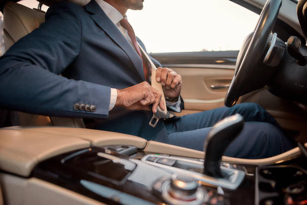 sicheres Fahren. geschnittenes Foto eines Geschäftsmannes in vollem Anzug, der auf einem Autositz sitzt und sich anschnallt - Foto, Bild