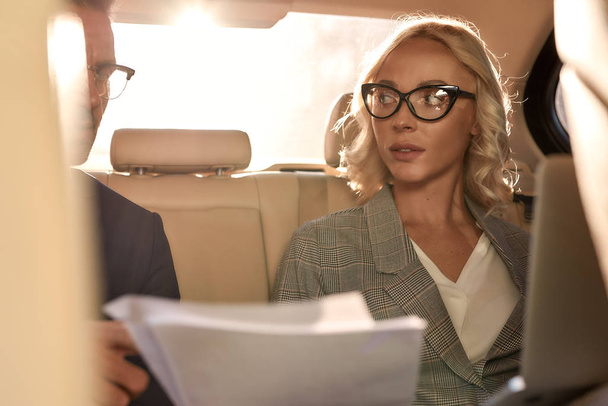 Listening carefully. Young and beautiful woman in eyeglasses looking at her business partner and discussing contract conditions while sitting in the car - Fotoğraf, Görsel