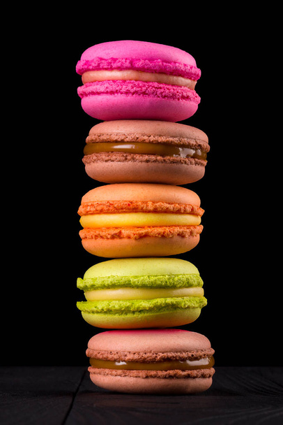 Row of french colorful macaroons or heap on wooden table isolated on black - 写真・画像