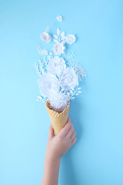 Hand holds a waffle cone with paper flowers on blue background. Holiday concept. - Photo, image