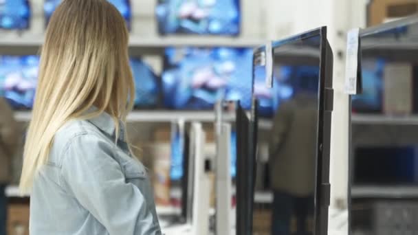 Smart modern female customer choosing large TV-sets at electronics store - Filmati, video