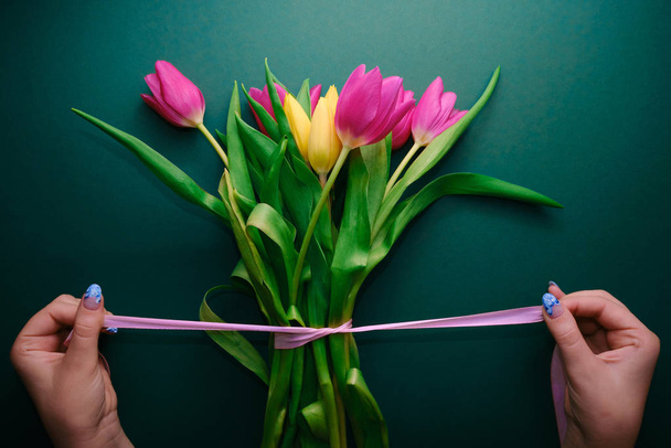 vrouw strikken roze lint op tulp bouqet, groene achtergrond, cadeau concept - Foto, afbeelding