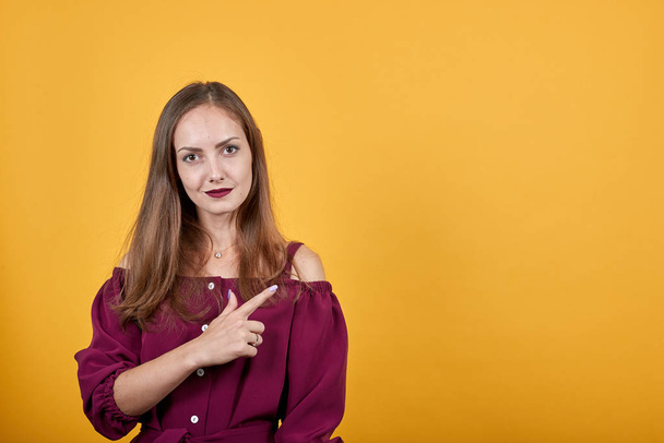 junge Dame in weinroter Bluse über isolierter orangefarbener Wand zeigt mit dem Finger nach rechts - Foto, Bild