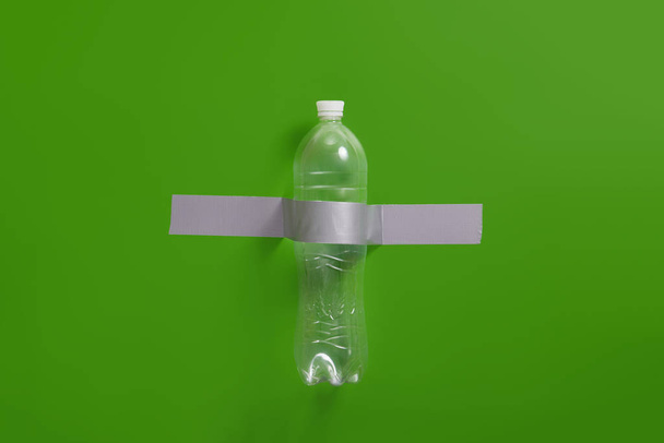 Transparent plastic bottle glued to the green wall with tape. Recycle concept - Foto, afbeelding