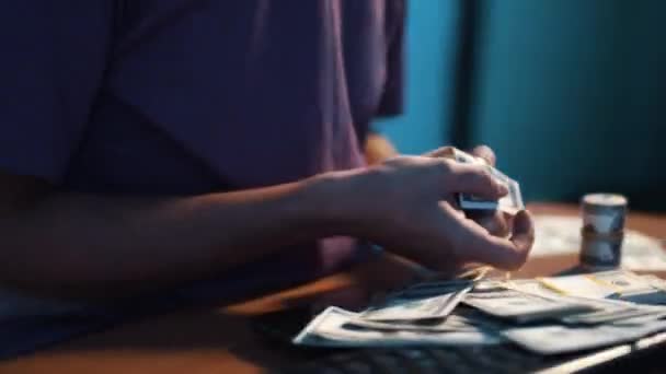 Man in t-shirt is carefully folding USA dollar bill sitting at desk in dark room - Filmagem, Vídeo