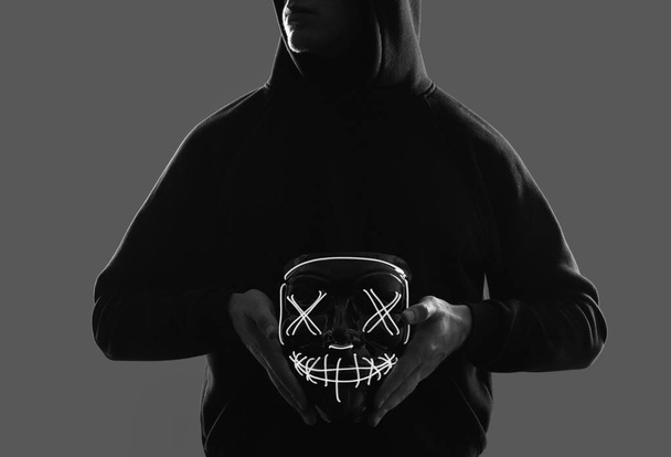 Anonieme man in zwarte hoodie verbergt zijn gezicht achter een neon masker - Foto, afbeelding