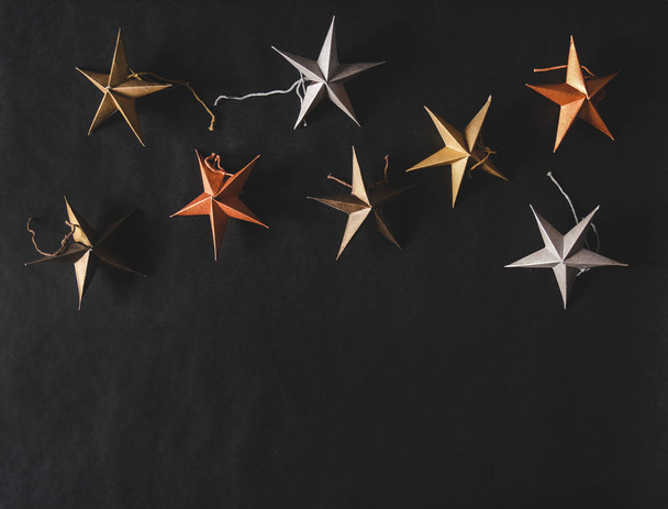Christmas or New Year holiday texture, wallpaper and background. Flat-lay of colorful paper toy decorative stars over black background, top view, copy space. Minimalistic concept - Fotó, kép