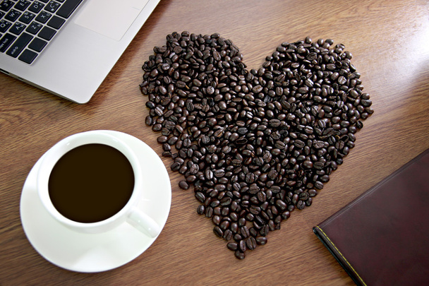 koffiebonen gerangschikt gevormd in een hart in de buurt van witte koffiekopje. - Foto, afbeelding