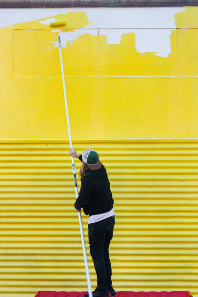 Duvarı sarıya boyuyorum, uzun bir fırçayla. - Fotoğraf, Görsel