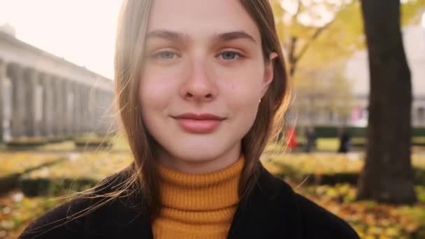 Porträt eines hübschen, fröhlichen Mädchens, das glücklich in die Kamera schaut und im Stadtpark bei Sonnenuntergang lächelt - Filmmaterial, Video