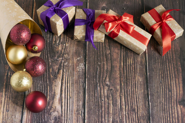 Χριστουγεννιάτικα δώρα, χρυσά, ασημένια, κόκκινα χριστουγεννιάτικα μπαλάκια χυμένα από ένα πακέτο χαρτί Κραφτ σε ξύλινο φόντο. Χριστουγεννιάτικα μπαλάκια. Αντιγραφικός χώρος - Φωτογραφία, εικόνα