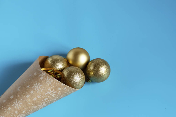 青い背景にクラフト紙のパッケージからこぼれた黄金のクリスマスボール。クリスマスボールコピースペース - 写真・画像