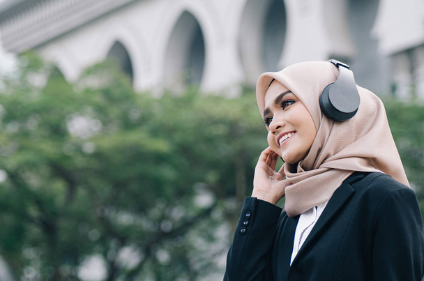 Πορτρέτο της όμορφης γυναίκας με μαύρο κοστούμι και χιτζάμπ χαμογελώντας ακούγοντας μουσική - Φωτογραφία, εικόνα