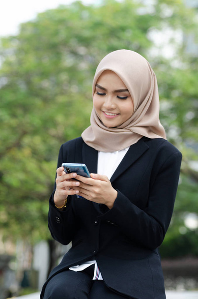 Портрет молодых бизнесвумен в черном костюме и хиджабе с помощью смартфона
 - Фото, изображение