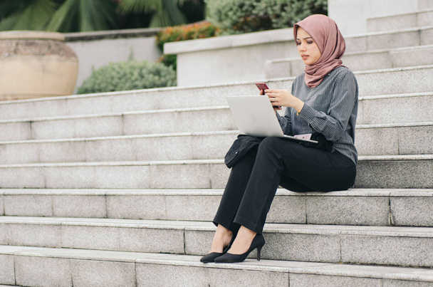 Beautiful asian businesswoman with laptop relaxing on stairs, and typing SMS   - Zdjęcie, obraz