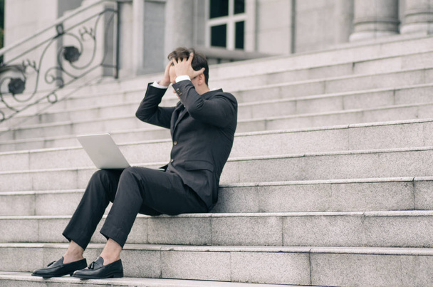 gefrustreerde en depressieve jonge zakenman zit op de trap terwijl het werken met zijn laptop - Foto, afbeelding