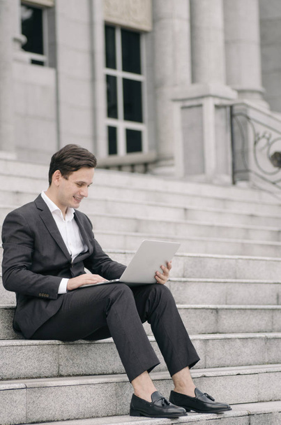 jeune homme d'affaires beau avec ordinateur portable relaxant sur les escaliers, se concentrer sur ordinateur portable avec sourire visage
 - Photo, image