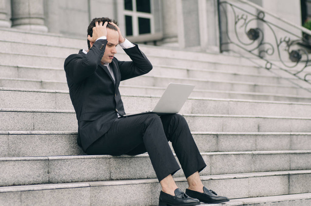 frustrovaný a depresivní mladý podnikatel sedí na schodech, zatímco pracuje se svým notebookem - Fotografie, Obrázek
