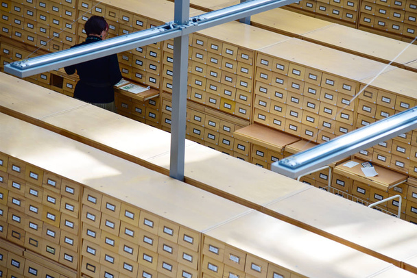 Библиотекарь среди деревянных шкафов с картотекой в библиотеке
 - Фото, изображение