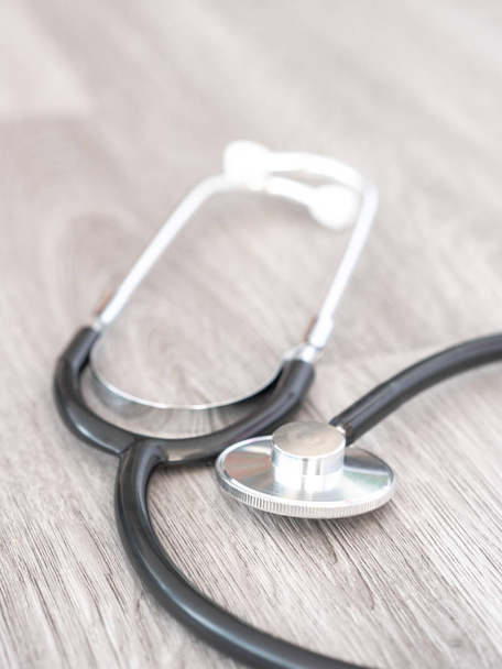 A doctors black flexible rubber and steel metal heart pulse stethoscope laying on a gray or grey wood grain floor or countertop background. - Photo, Image