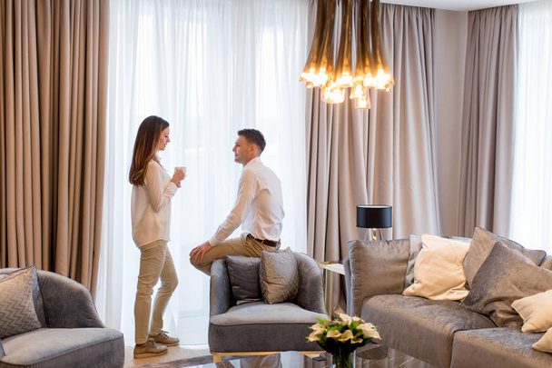 Nuori pari rentouttava ja puhuu kahvikupit ylellinen huone nykyaikainen huoneisto
 - Valokuva, kuva