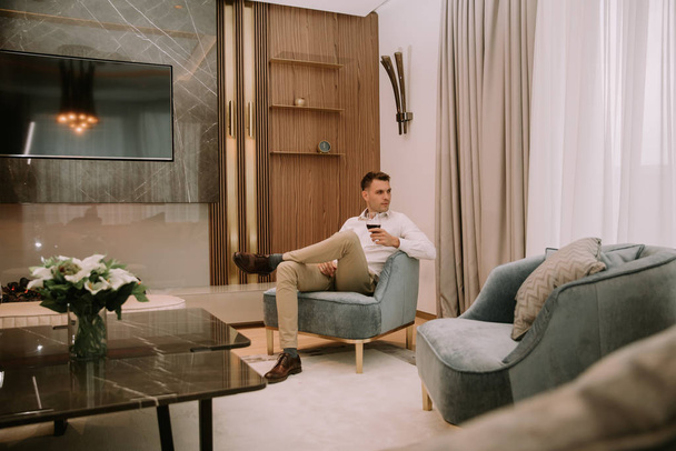 Młody mężczyzna siedzi w luksusowym apartamencie, pije czerwone wino i relaksuje się - Zdjęcie, obraz
