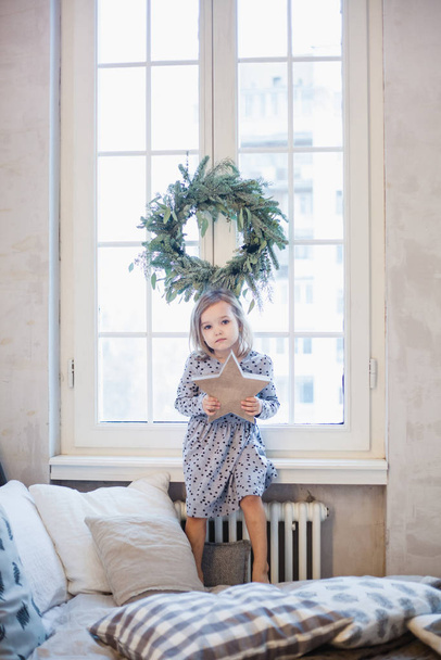 Fille près de la fenêtre tenant une étoile en carton, la chambre est décorée pour la nouvelle année et Noël
 - Photo, image