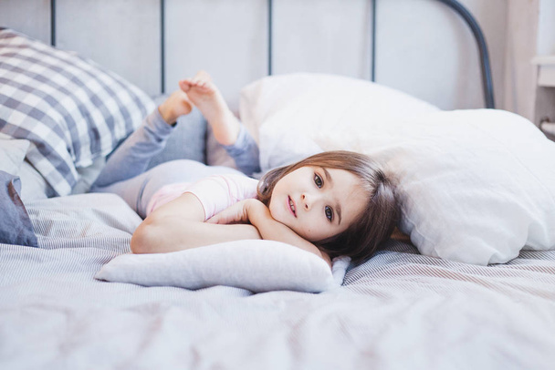Mädchen liegt auf dem Bett, kleines Mädchen ruht zwischen Kissen und Decken, träumt - Foto, Bild