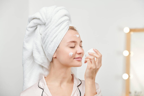 Agradable chica bonita disfrutando del olor de la crema facial mientras cuida su cara y cuerpo por la mañana
 - Foto, imagen