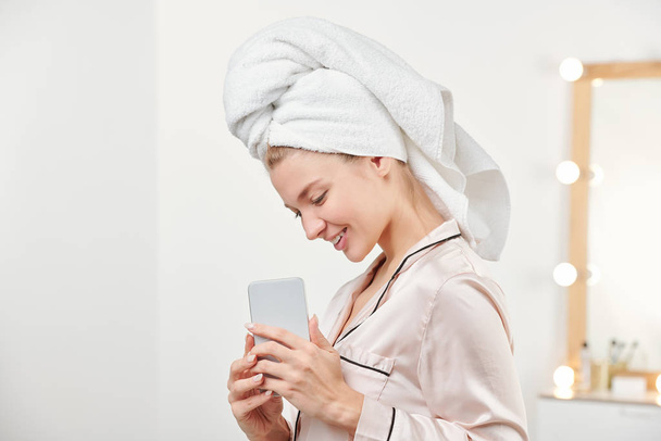 Menina muito sorridente com toalha na cabeça segurando smartphone na frente de si mesma enquanto fotografa algo
 - Foto, Imagem